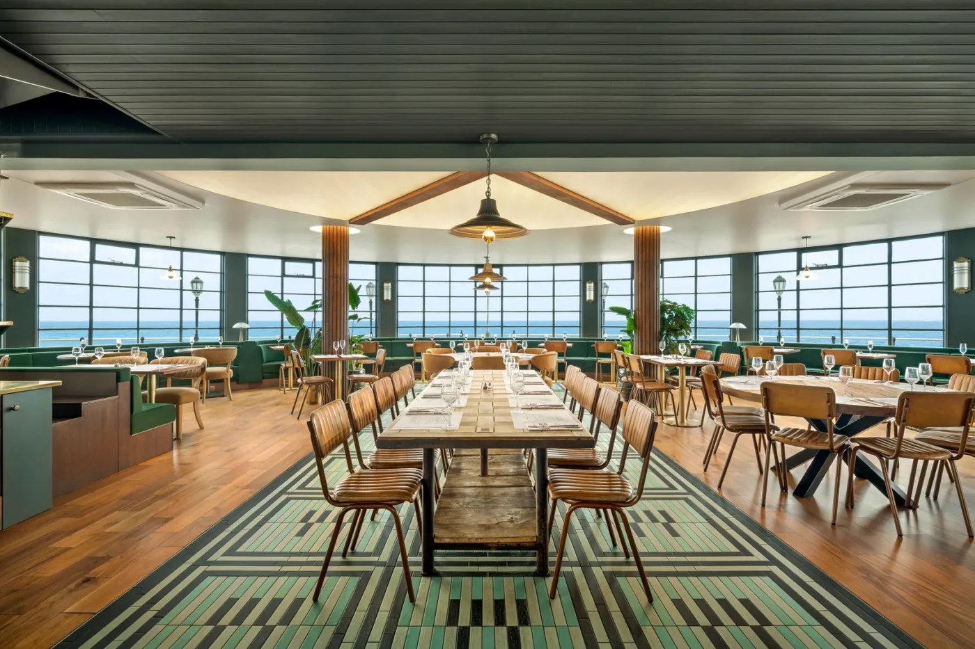 Inside Perch on the Pier, green banquettes, large central dining table, sea view through arched windows